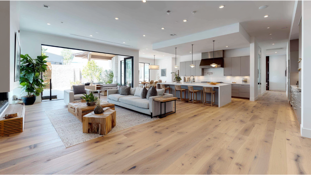 Spacious open-concept home with light natural wood flooring, modern furnishings, large kitchen island, and sliding glass doors leading outside.